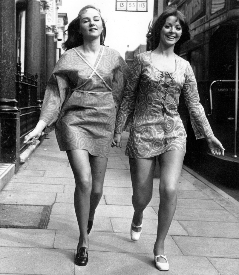 Moya Gillett, left, and Lina Huby hold hands as they walk in their paper mini-dresses on a sidewalk in London, England on April 7, 1970.